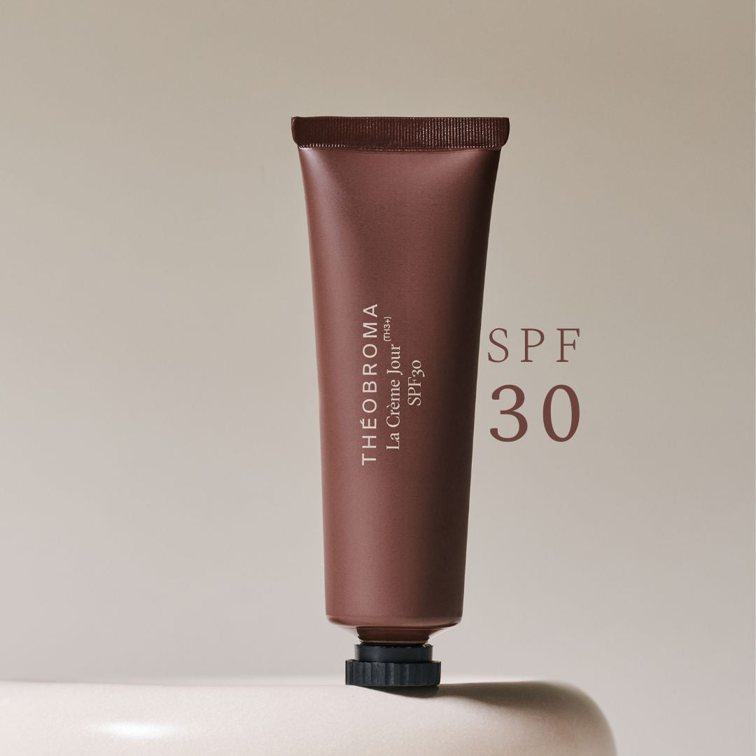 Tube de crème de jour Théobroma avec SPF 30, couleur marron, posé à l’envers sur un support beige, avec un fond neutre élégant, pour une peau lisse et éclatante